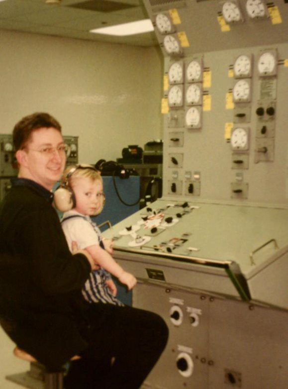 Jonathan Haymans in front of a simulator for the EPCP electric plant control panel with young son helping